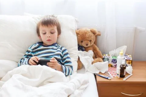 Sick child boy lying in bed with a fever, resting Stock Photos