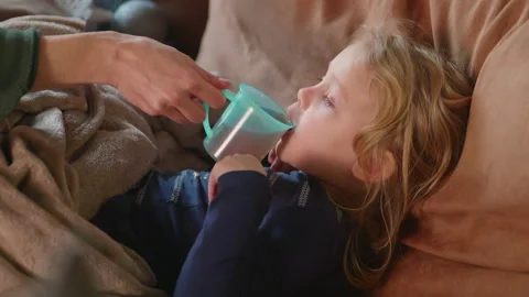Sick child gets her warm drink while lying on the sofa with fever, getting well Video stock 230982027