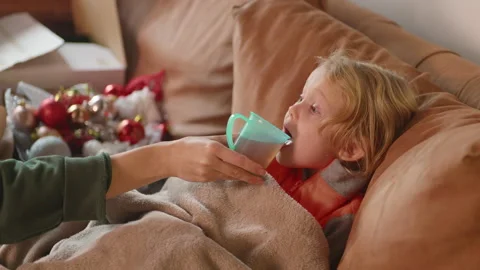 Sick child gets her warm drink while lying on the sofa with fever, cozy blanket Stock Footage 231463463