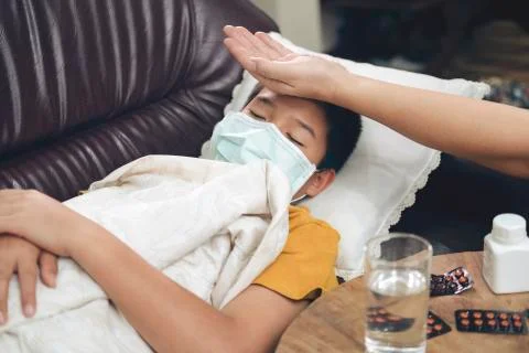 Sick child lying in sofa bed with protection mask on face against infection Stock Photos