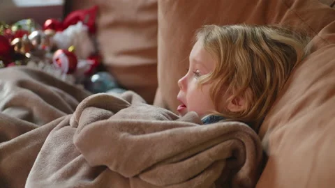 Sick child resting on the sofa under blanket, struggling of fever, watching tv Stock Footage 230861874