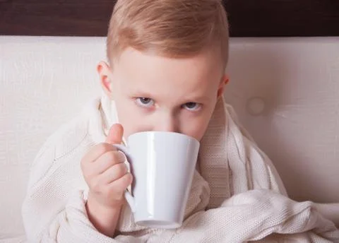 The sick child sitting in a bed and holds a cup of tea. Medicine concept. Stock Photos
