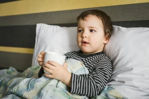 Sick curing boy with cup of medicament lying on bed Stock Photos