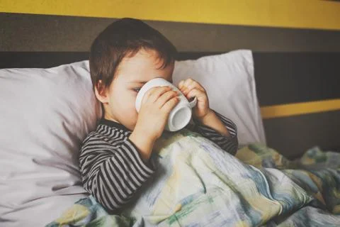 Sick curing boy lying on bed drinking medicament Stock Photos