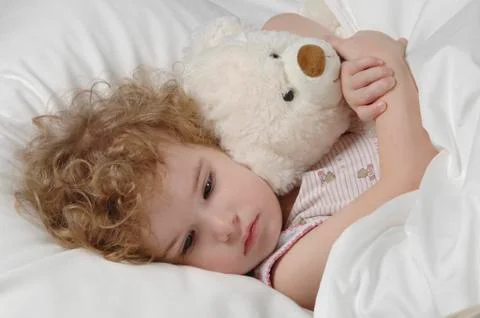 Sick girl lying in bed with teddy bear Stock Photos