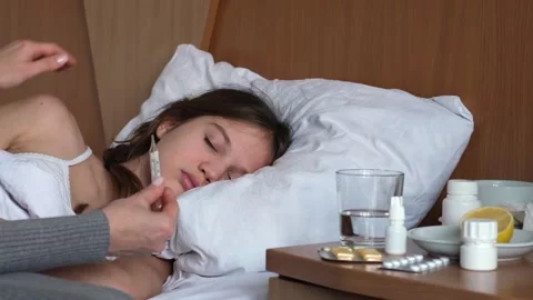 Sick girl with thermometer lying in bed and mother taking her temperature Stock-Footage 301894063