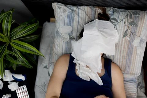 A Sick Individual Lying in Bed Resting while Holding a Tissue for Comfort and Stock Photos