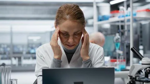 Sick lab expert rubbing head temples, feeling ache while working on laptop Stock Photos