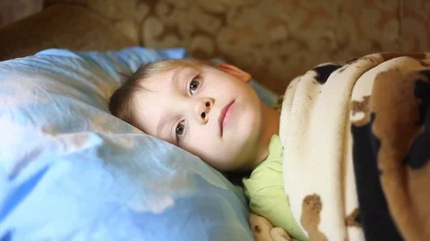 Sick little boy, lying in bed with a flu and a fever, watching TV Video stock 74490019