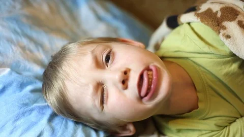 Sick little boy, lying in bed with a flu and a fever, watching TV Video stock 74490069