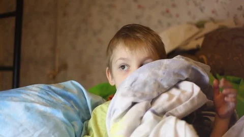 Sick little boy, lying in bed with a flu and a fever, watching TV Stockbeeldmateriaal 74490084