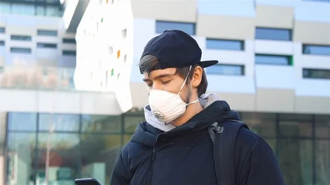 Sick ma in respiratory mask using telephone standing alone on the street Stock Footage 129929857