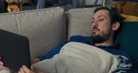 Sick man with beard is lying on sofa and covered with blanket. Man with dark 스톡 동영상 218323973