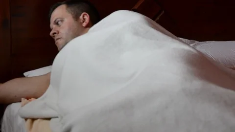 Sick man in bed measures the temperature and coughs Видео 126717715
