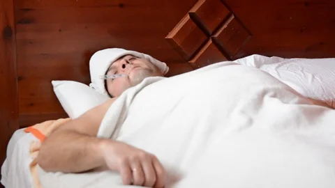 Sick man in bed measures the temperature and coughs Видео 126721897