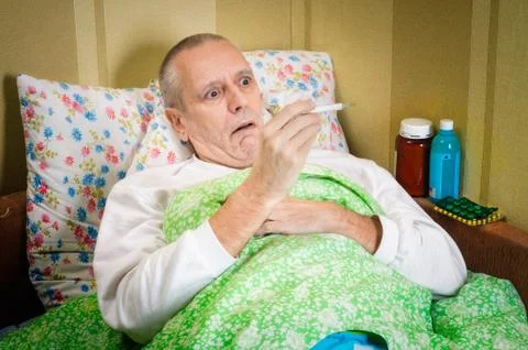 Sick man in bed with thermometer Stock-Fotos