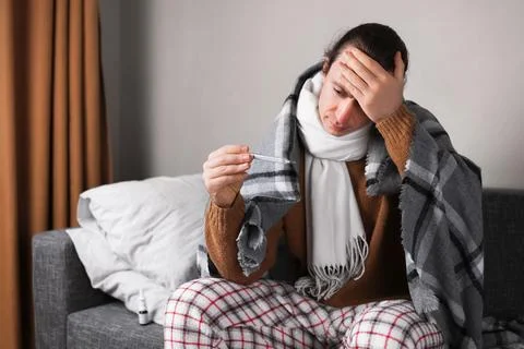 Sick man in blanket checking temperature with thermometer and touching fore.. Foto stock