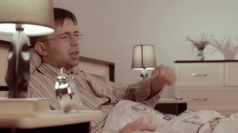 Sick man checking his fever and sneezing in bed Видео 68421204