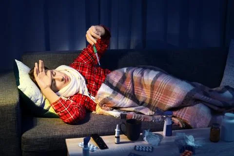 Sick man checking his high fever on the sofa at home, suffering from a hard.. Stock Photos