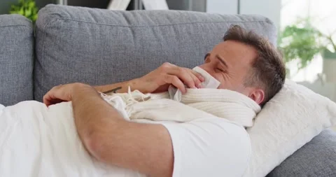 Sick man with cold and fever resting on sofa, blowing nose with tissue at home Video stock 322220411