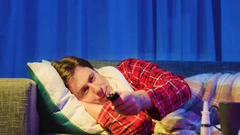 Sick man with a cold and flu resting at home. He watches television on a couch w Stock Footage 342811159