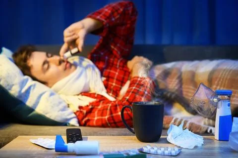 Sick man with cold and flu symptoms uses nasal spray on a couch. Home treat.. Stock Photos