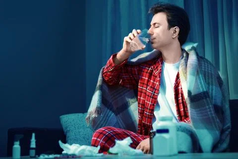 Sick man with cold and flu illness drinks water for recovery and treatment .. Stock Photos