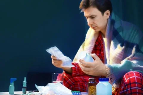 Sick man with cold and flu symptoms reading medicine instructions for home .. 库存照片