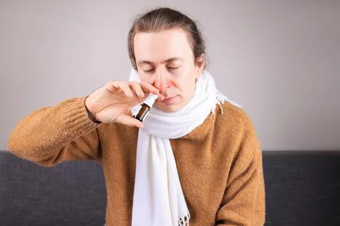 Sick man with cold and red nose using nasal spray bottle to treat congestio.. Stock Photos
