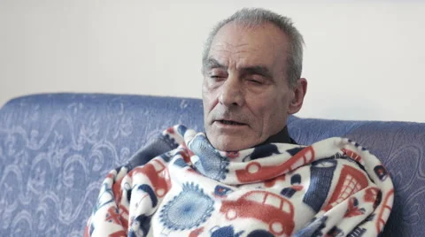 Sick man with colds and flu sits on the couch wrapped in a blanket Stock Footage 47826839