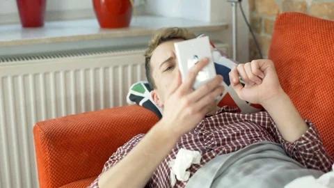 Sick man coughing while lying on the sofa and using smartphone, steadycam shot Stockbeeldmateriaal 70856121