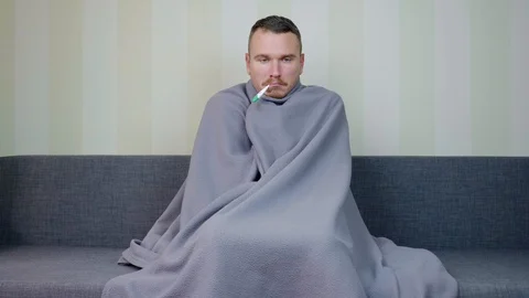 Sick man covered with blanket measures the temperature with thermometer Stock Footage 119515980