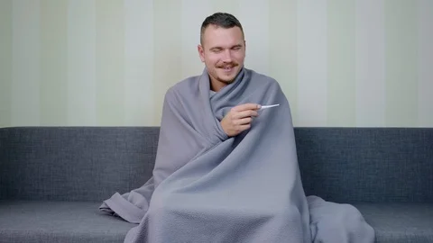 Sick man covered with blanket measures the temperature and enjoys a good result Video stock 119516309
