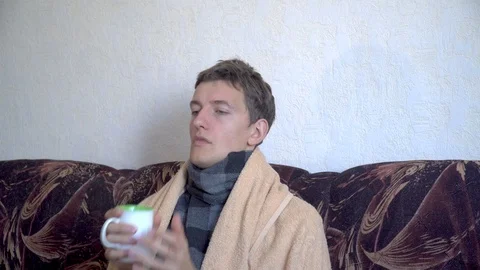 Sick man drinking tea with lemon sitting on couch at home Stock Footage 118766450