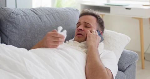 Sick man with fever on couch calling doctor, holding tissue during flu season Video stock 326981672