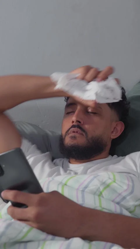 Sick man with fever lying in bed using smartphone Video stock 329124299