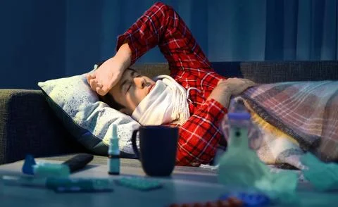 Sick man with a fever lying down with a cold and flu during home care. Tabl.. Stock Photos