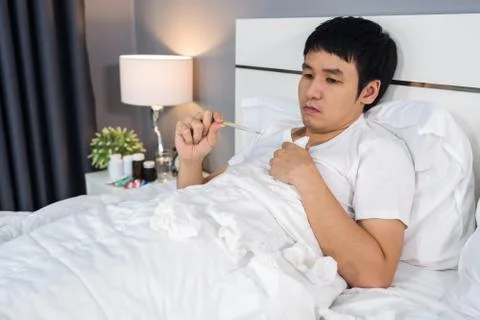 Sick man is headache and using thermometer to checking his temperature in bed 写真素材