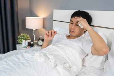 Sick man is headache and using thermometer to checking his temperature in bed 写真素材