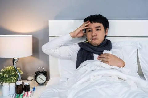 Sick man is headache and using thermometer to checking his temperature in bed Stock Photos