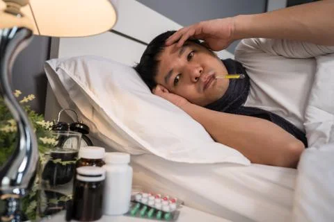 Sick man is headache and using thermometer to checking his temperature in bed Stock Photos