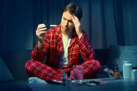 Sick man holding a thermometer checking high fever from cold and flu. Home .. Stock Photos