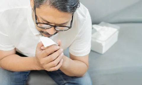 Sick man holding a tissue while coughing in the living room. Sore throat an.. Stock Photos