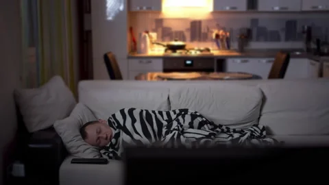 Sick man lies in the evening on the couch by the TV and coughs, camera movement Stock Footage 131747429