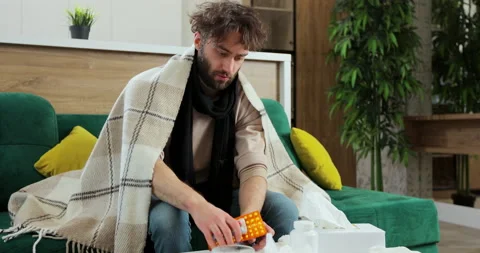Sick man looking at pills, trying to cure virus disease at home. Young man with Видео 168472198