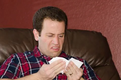 Sick man looking at a tissue after blowing his nose. Stock Photos