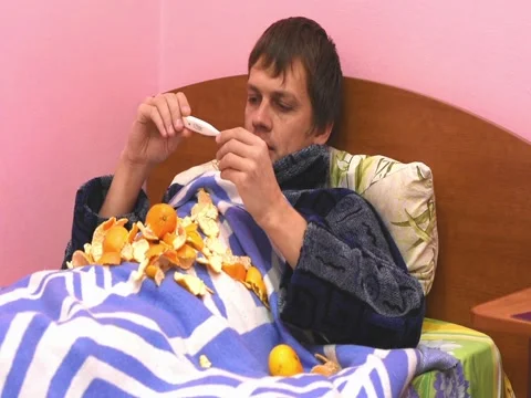A sick man lying in bed, measuring the temperature and eats tangerines Stock Footage 70071717