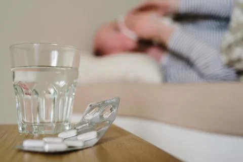 Sick man lying in bed with pills and glass of water Stock Photos