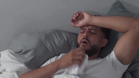 Sick man lying in bed suffering from a fever Stock Footage 329123867