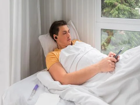 Sick man is lying in bed with thermometer. Man is searching online for diseas Stock Photos